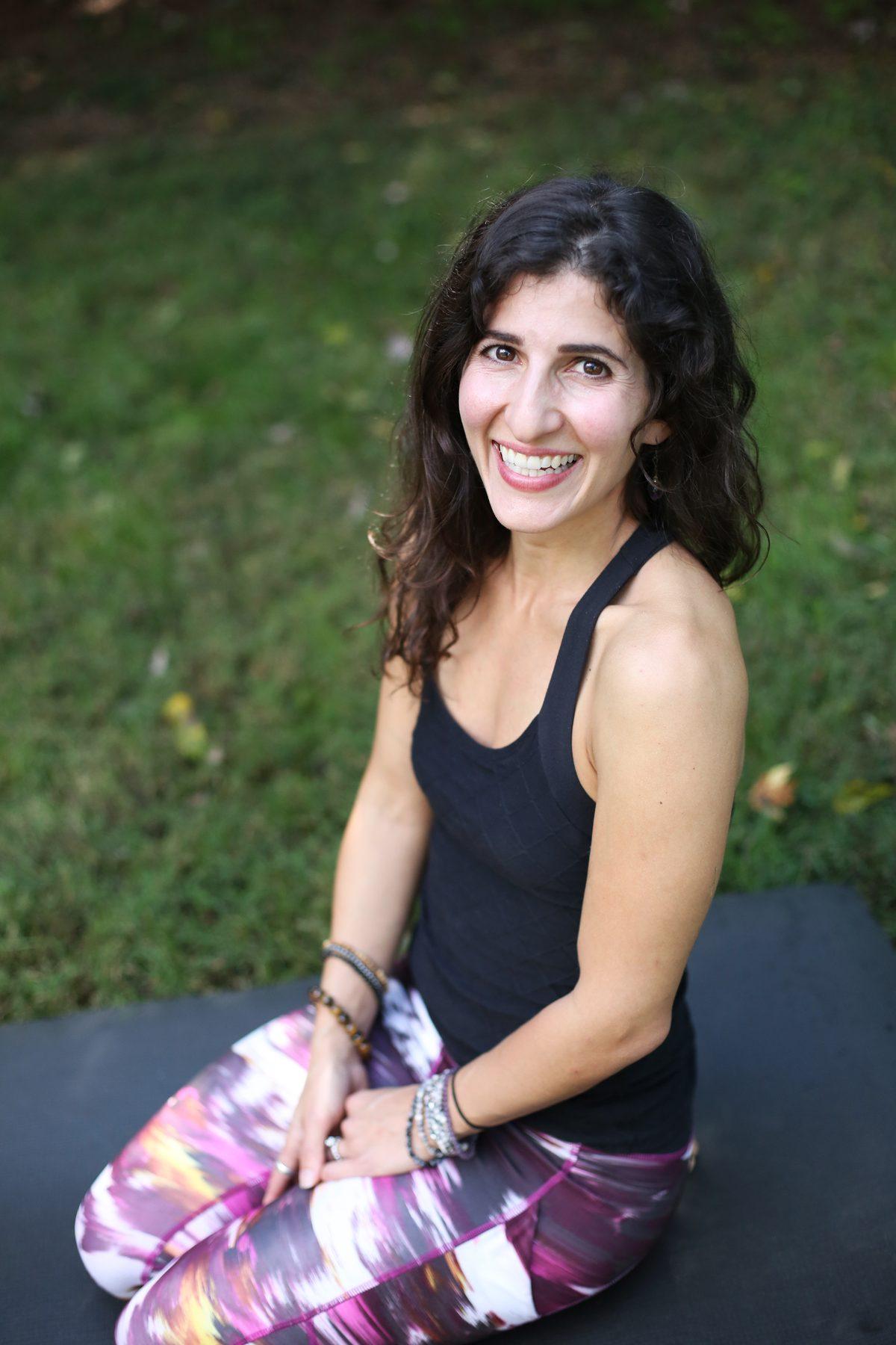 Maro smiling, seated outdoors on her mat